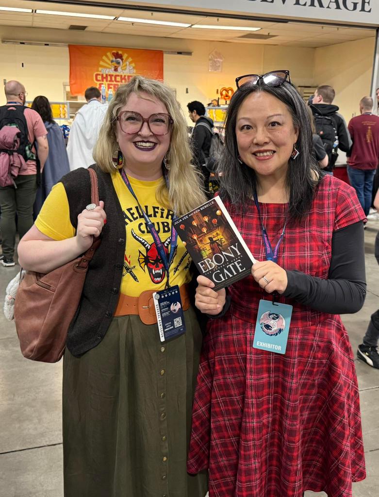 Julia Vee at Dragonsteel Nexus 2025 with librarian, holding a copy of Ebony Gate.